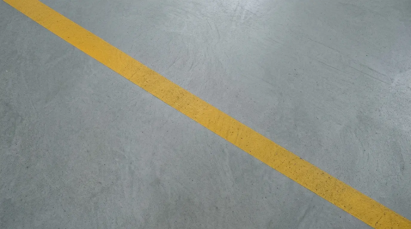 Uma linha amarela recém-pintada atravessando na diagonal um piso de concreto limpo.